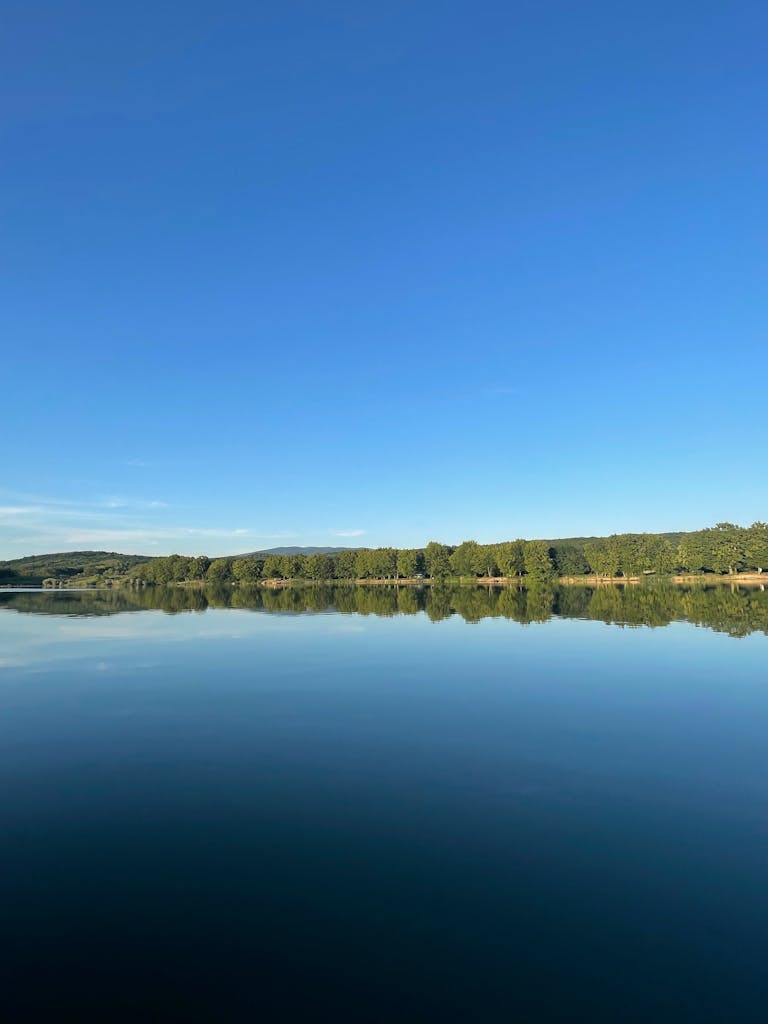 A tranquil lake with clear blue sky and lush green shore reflecting perfectly in the water.