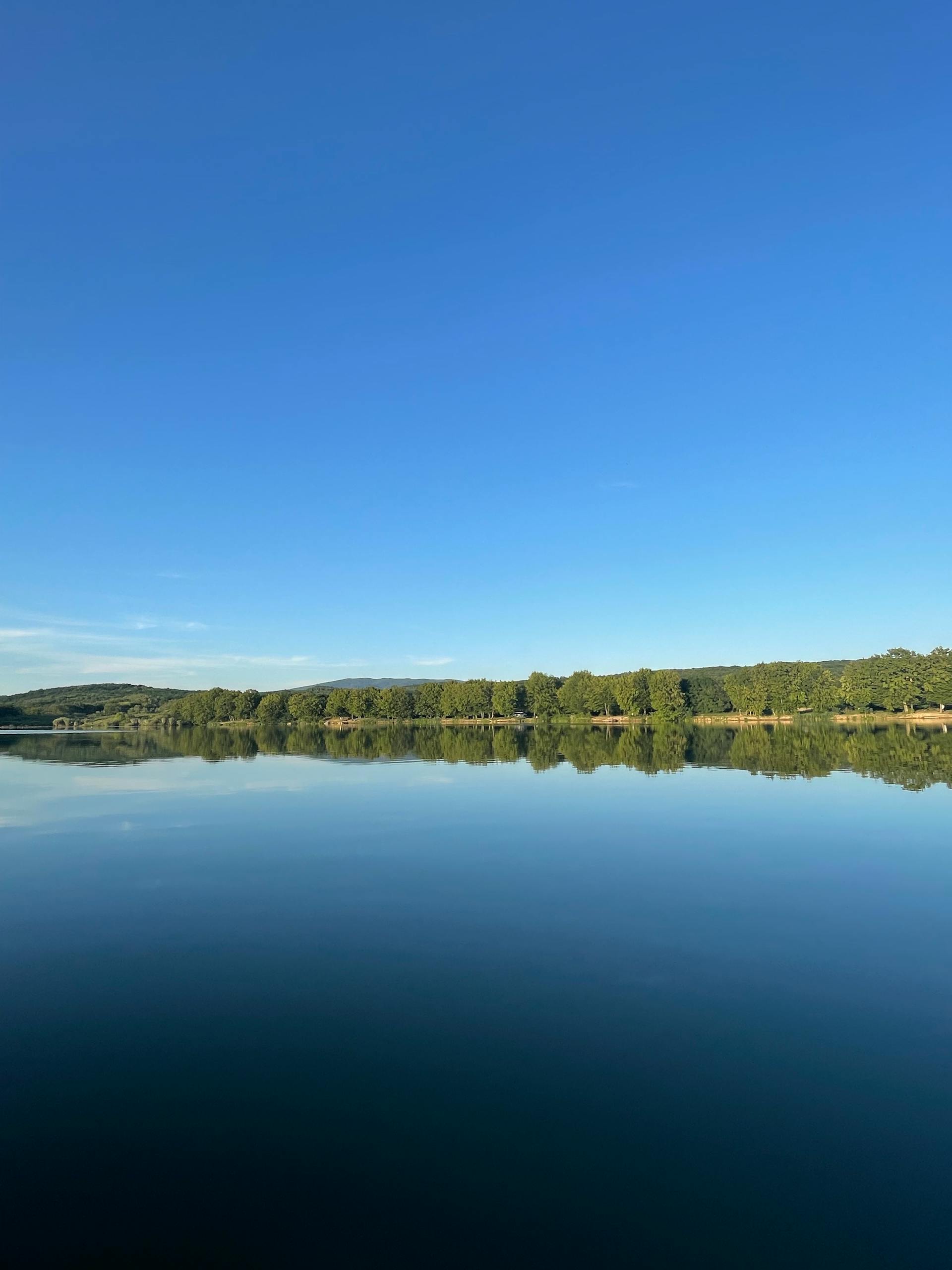 A tranquil lake with clear blue sky and lush green shore reflecting perfectly in the water.