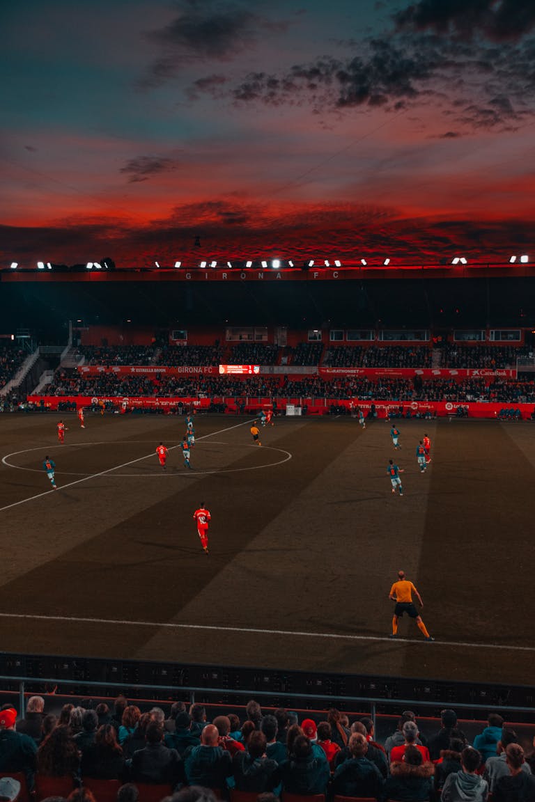 Wide-angle view of a soccer match taking place in a stadium at sunset with a vibrant sky.